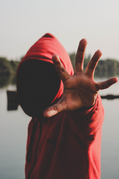 man in a red hoodie shading his face stretching his hand out to stop the camera