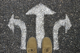 pair of feet from above on asphalt with arrows chalked up and away in different directions