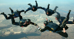 group of six skydivers in formation, hands locked in a ring