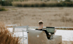 man from behind sitting on a comfy chair in nature with his laptop on his lap