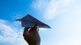 silhouette of a hand against the blue sky, preparing to throw a paper airplane