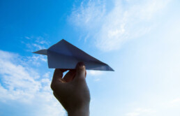 silhouette of a hand against the blue sky, preparing to throw a paper airplane