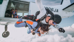 two people jumping out of a plane, one clipped to the front of the other