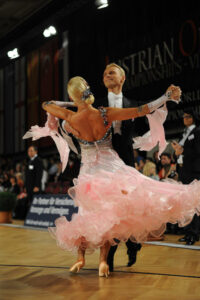 a man in a suit and a woman in a ruffly pink dress waltzing