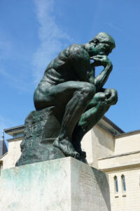 looking up at Rodin's The Thinker with the blue sky behind him