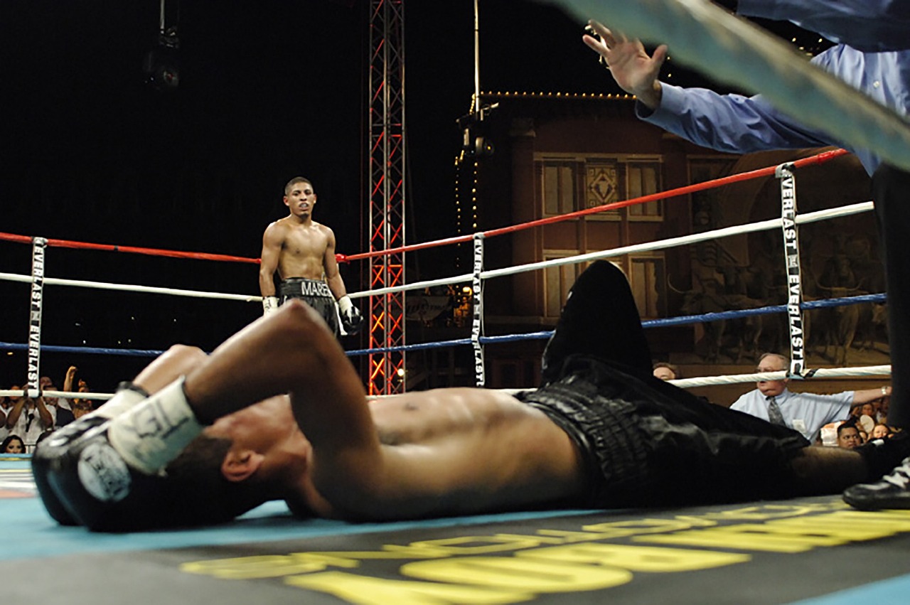 a boxer standing triumphant over his opponent who's lying on the ground, head in his hands